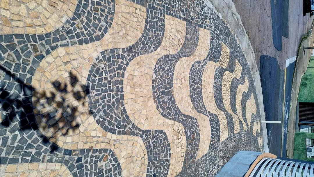 Calçada de ondas amarela e preto de pedras usadas.