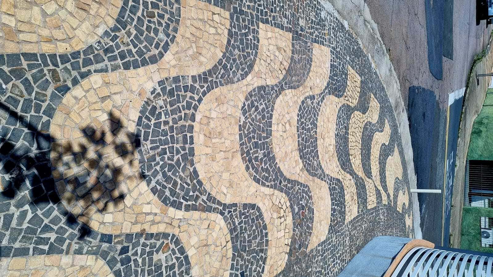 Calçada de ondas amarela e preto de pedras usadas.